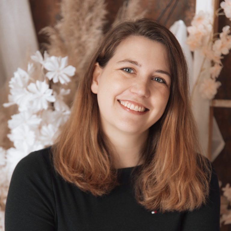 Mara Belger - Schicksalserbin Porträt einer Frau mit langen, glatten, braunen Haaren und einem lächelnden Gesicht.